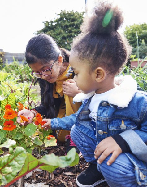 two girls sniffing flowers in garden