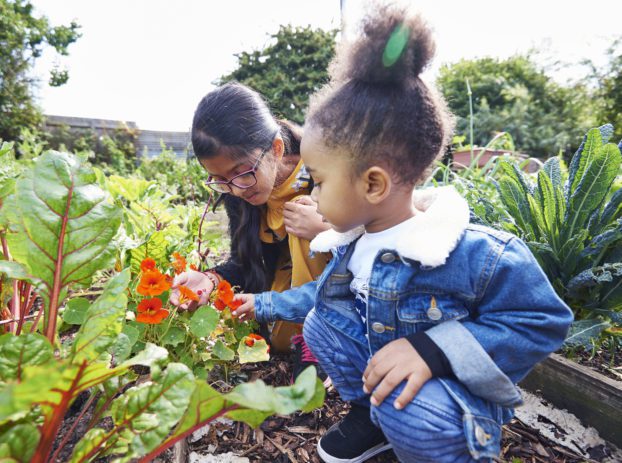 two girls sniffing flowers in garden