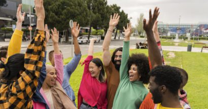 Multiracial group of several young people raising their hands happily. Celebrating outdoors.